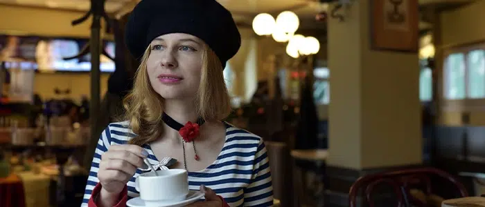 Mujer usando una boina francesa mientras sostiene una taza de café.