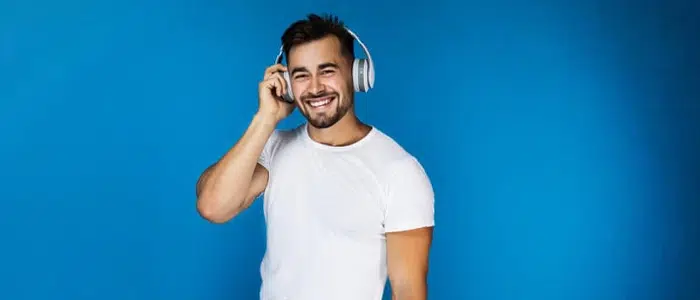 Hombre con camiseta blanca sonriendo con audífonos puestos.