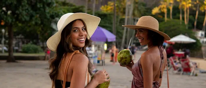 Dos mujeres vistiendo outfits tropicales mientras disfrutan de un coco en la Isla Dominica.