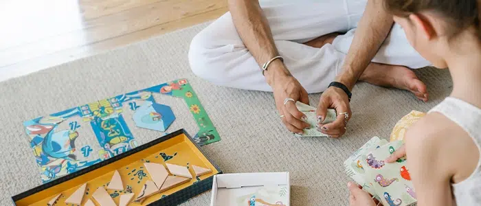 Un adulto y una niña divirtiéndose con un jjuego de cartas, sentados en una alfombra.