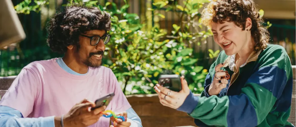 dos amigos sentados afuera riendose con sus telefonos en la mano