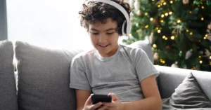 Niño con audífonos de diadema puestos usando un celular para jugar